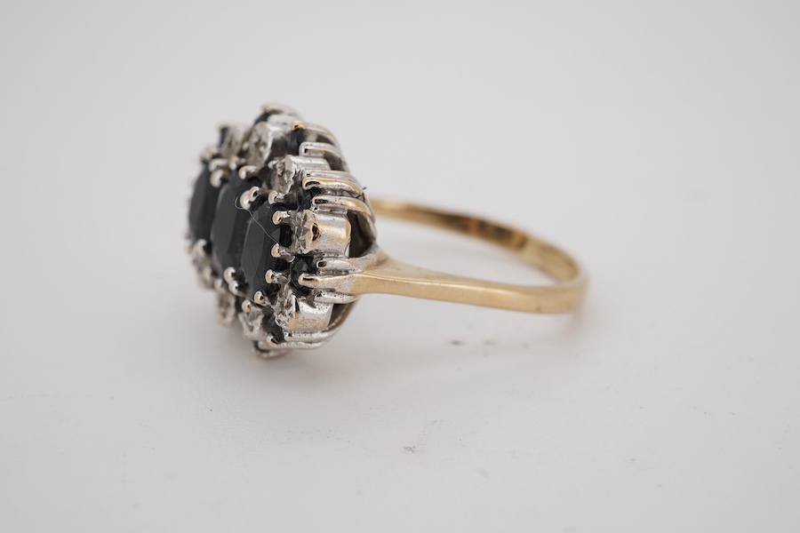 A modern 9ct gold and three stone sapphire set dress ring, with sapphire and diamond chip set border, size Q.